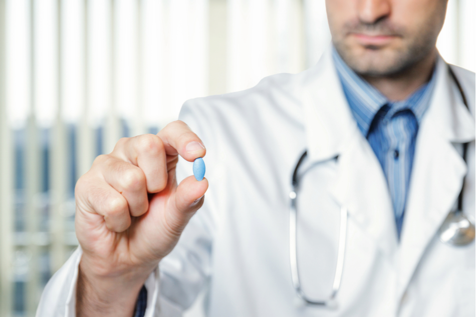 Doctor holding generic blue pill between his fingers