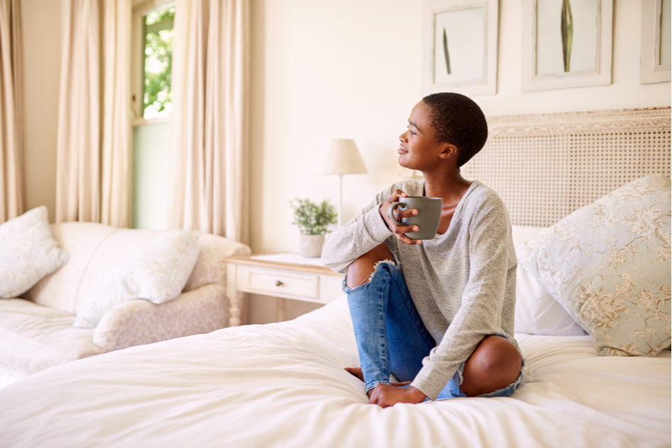 young beautiful Black woman sits on bed with a cup of tea