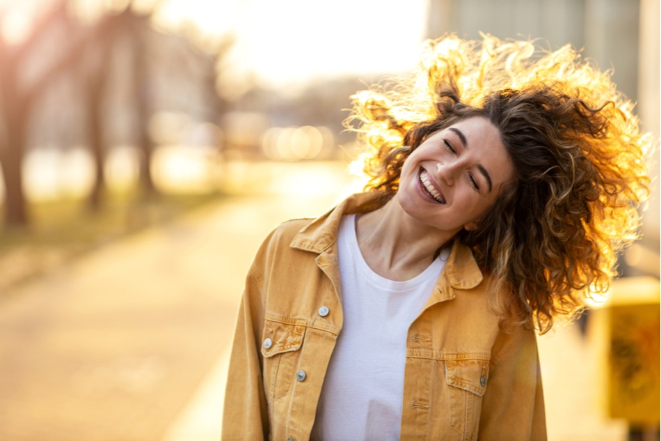 happy woman outside with yellow jacket and voluminous curly hair