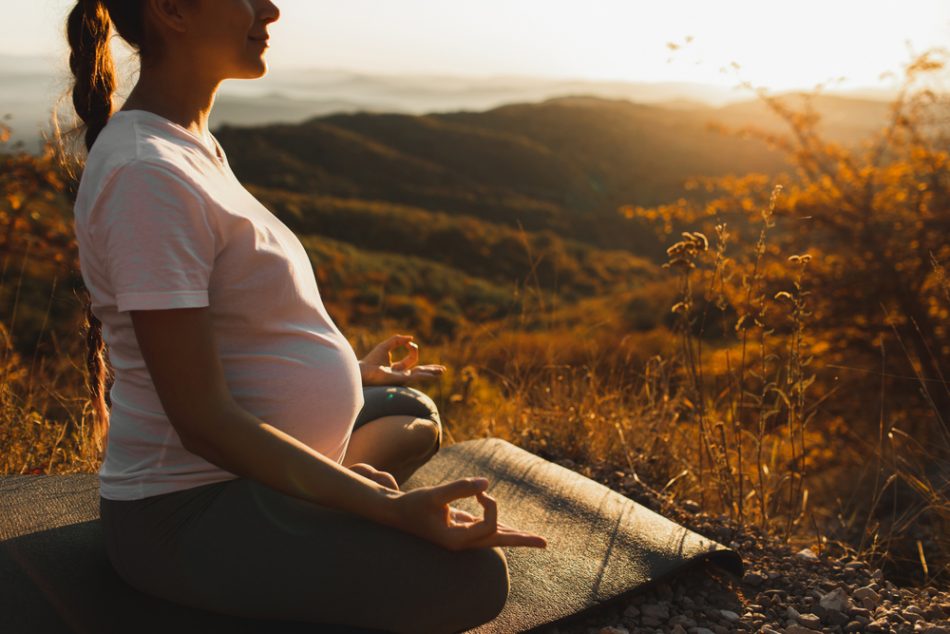 Pregnant woman does yoga on a hill at sunset
