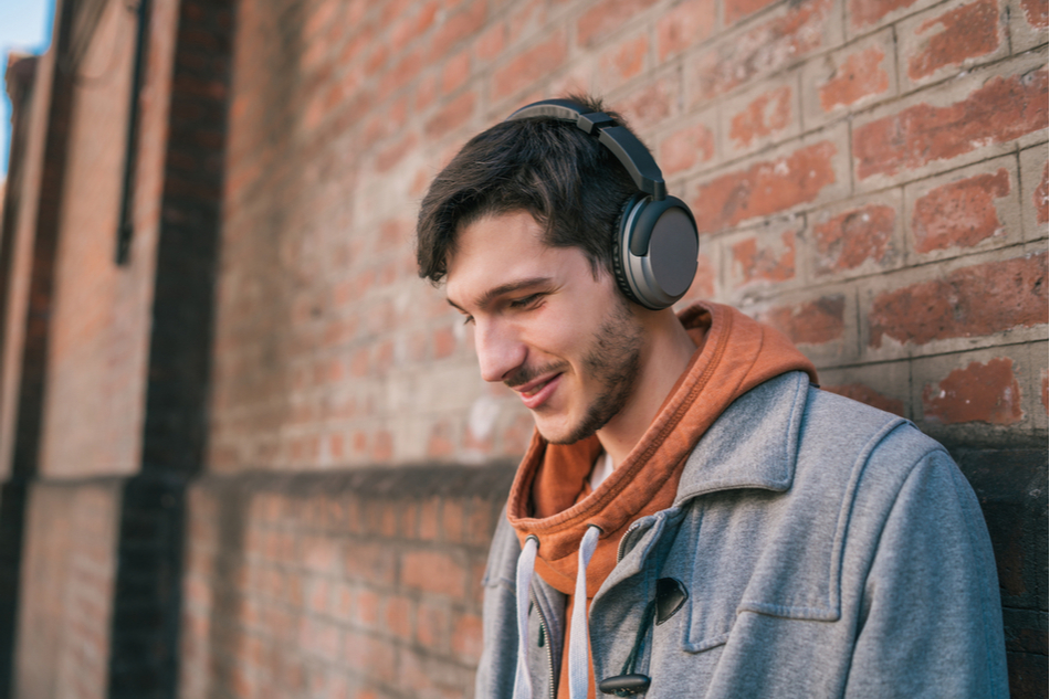 Man listens to music through headphones while standing against brick wall