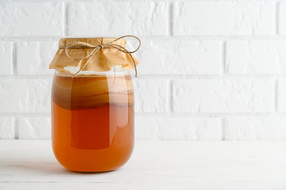 Homemade fermented kombucha tea in a glass jar on a background of a white brick wall.