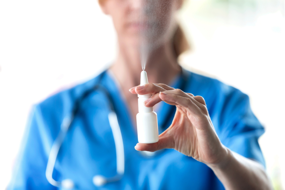 Nurse dressed in blue scrubs with stethoscope spraying nasal spray