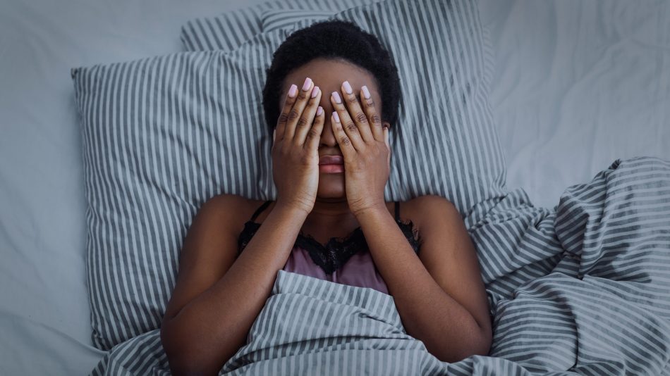 young black woman covers eyes while laying in bed