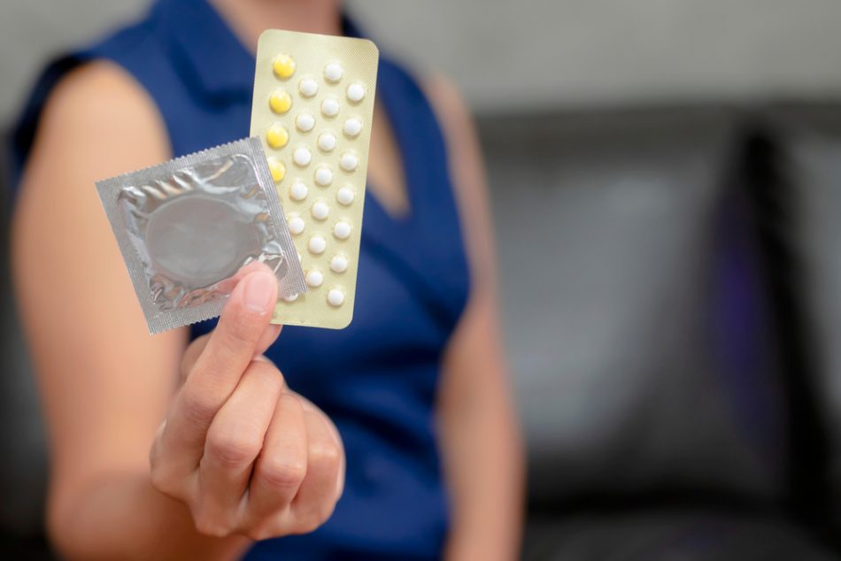 Woman hand holding contraceptive pills and condom sitting on sofa background,protection, safe sex,contraceptive means.