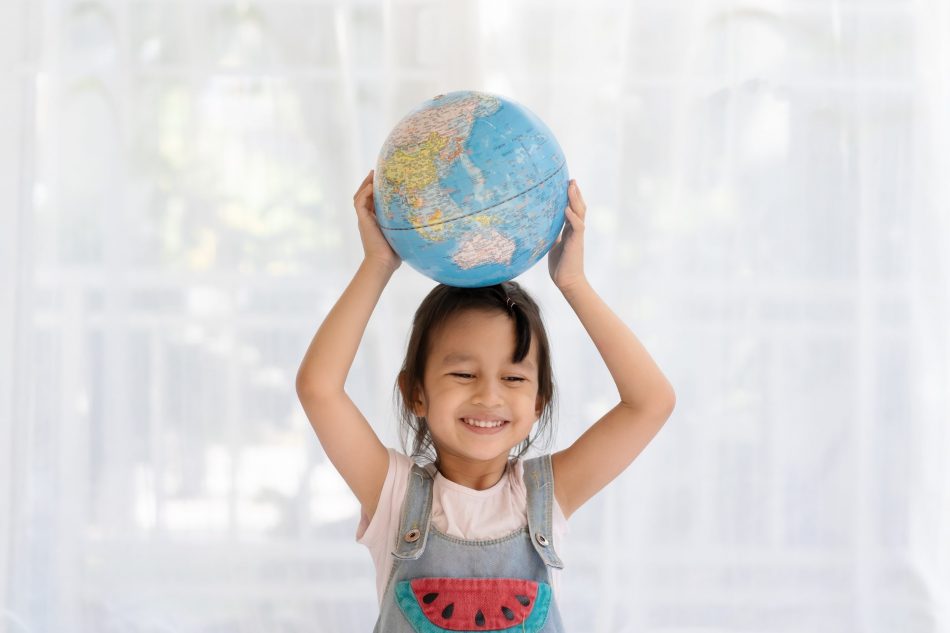 Happy and healthy asian little girl is raising the globe model