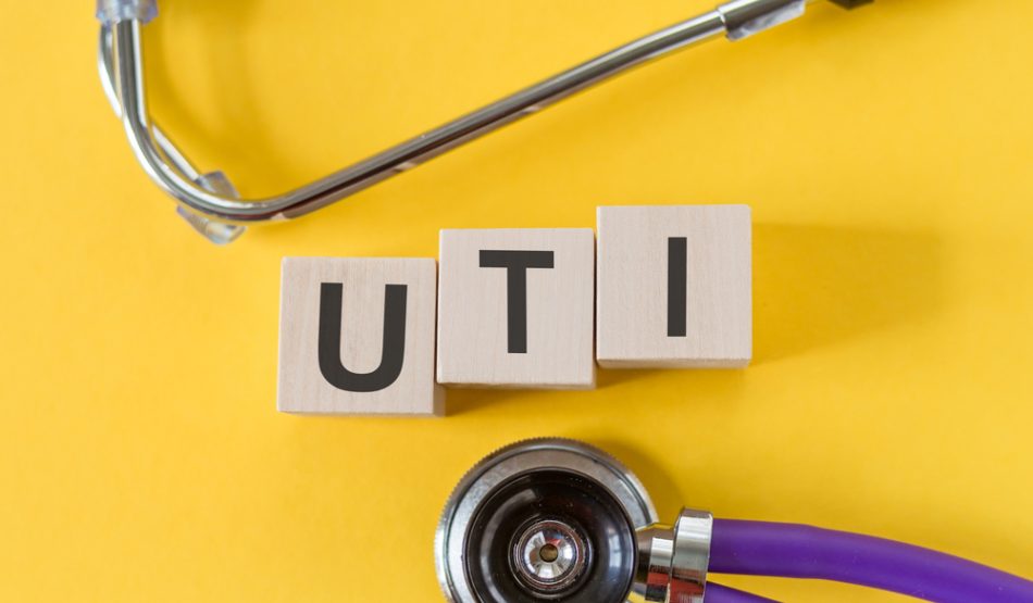 UTI - acronym from wooden blocks with letters, abbreviation UTI urinary tract infection, concept, yellow background with stethoscope.