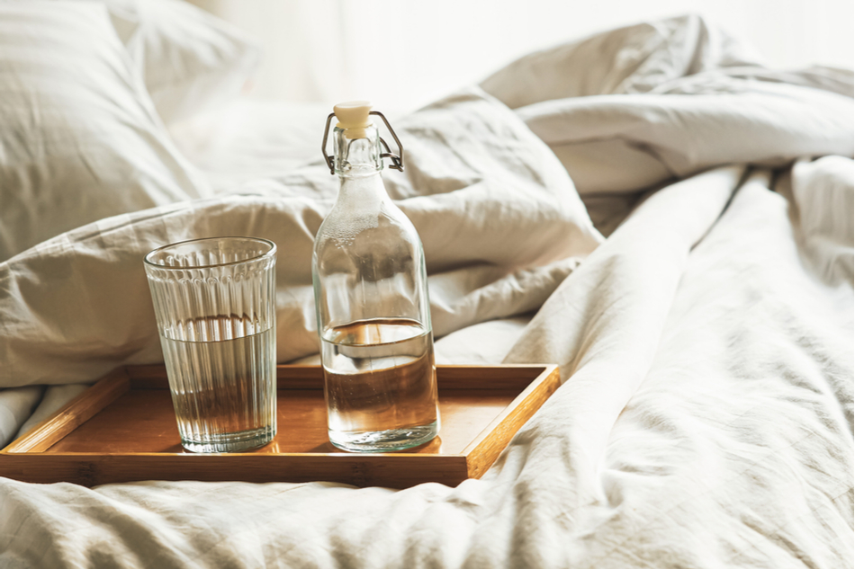 bottle of water next to glass of water sitting on a tray placed on white bed