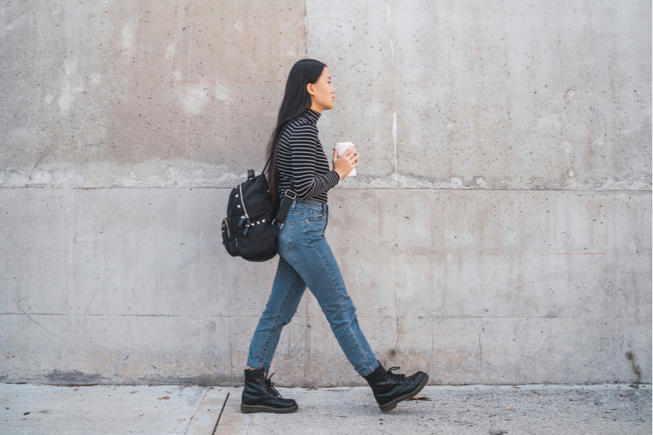 full side view of Asian American woman walking against grey wall