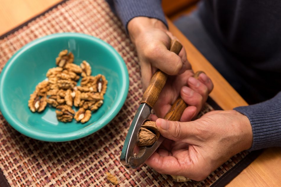 hands peeling walnuts in a blue bowl.