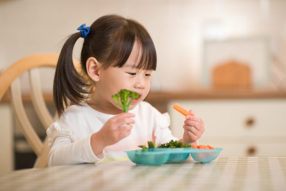 Young girl eating carrots and broccoli