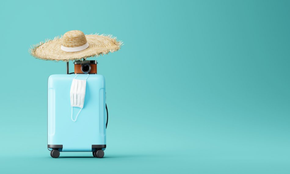 Blue suitcase with face mask and travel accessories on blue background