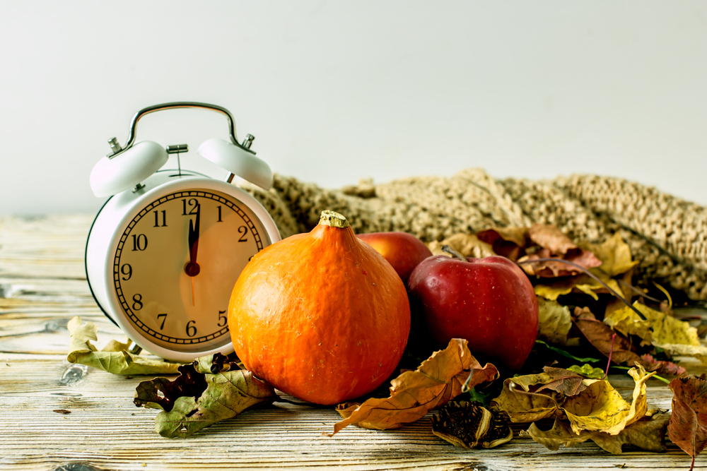 Old-fashioned clock next to pumpkin and fall foliage