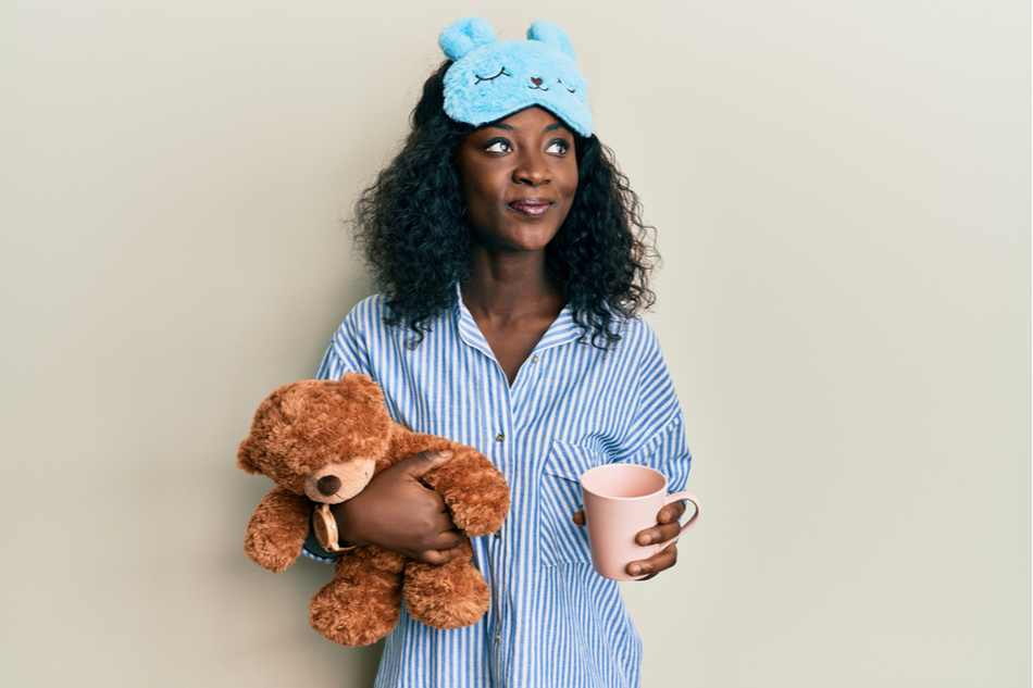 Young Black woman in sleepwear and sleeping mask holding a teddy bear