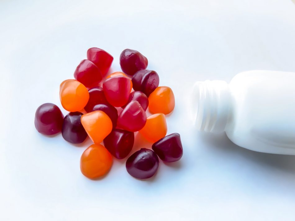Group of red, orange and purple multivitamin gummies with the bottle isolated on white background.