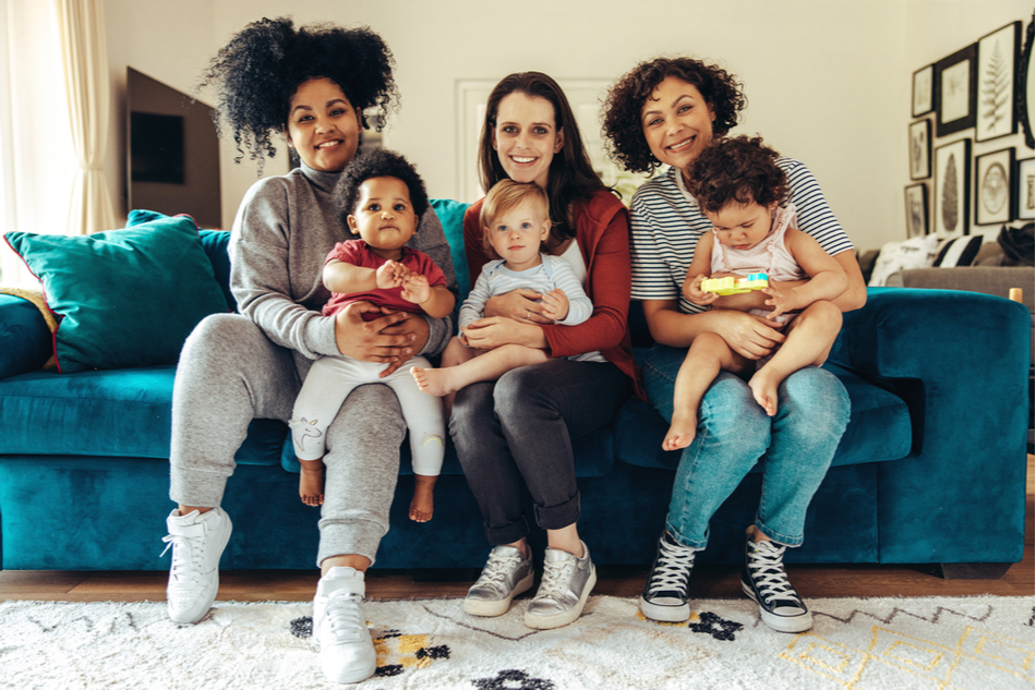 three diverse mothers sit on a couch with their infants