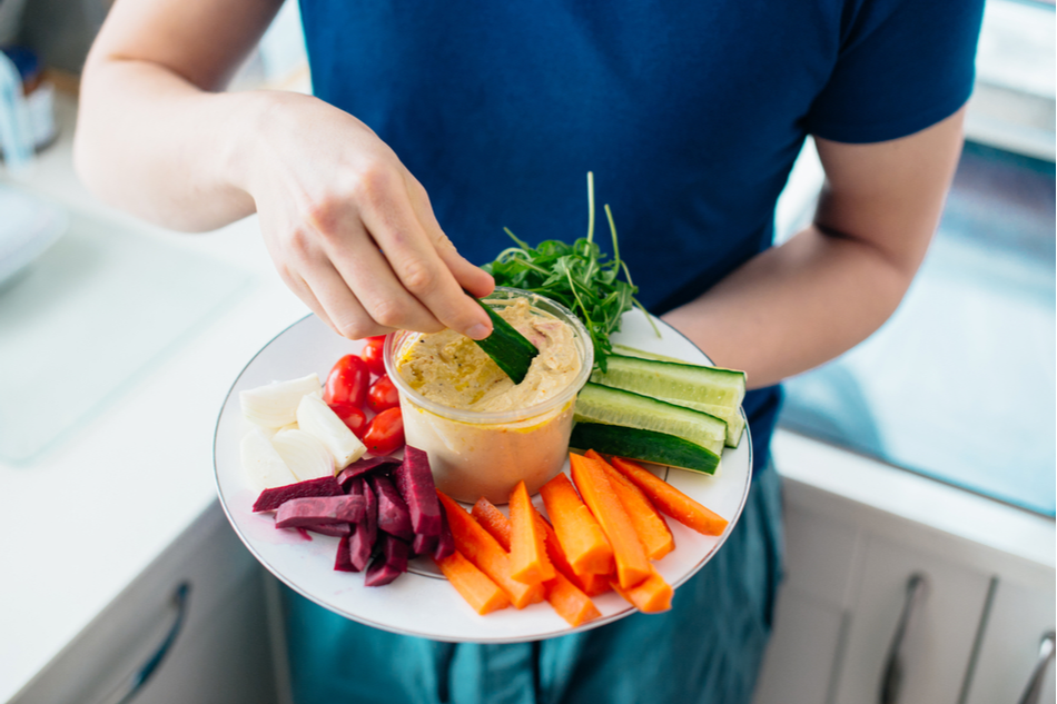 top view of man's torso holding plate of veggies and hummus