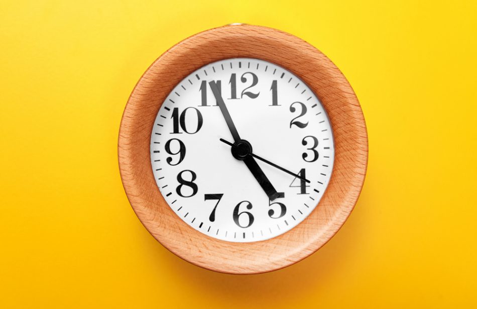 Wooden round clock on yellow background showing the concept of five minutes.