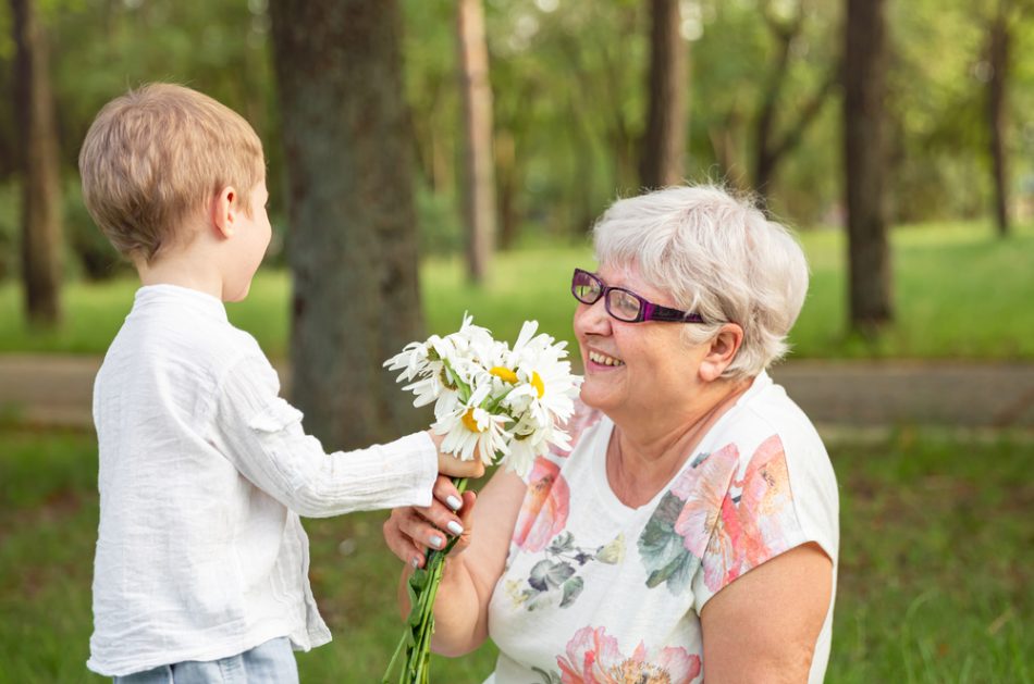 Boy giving white and yellow flowers to elderly woman.