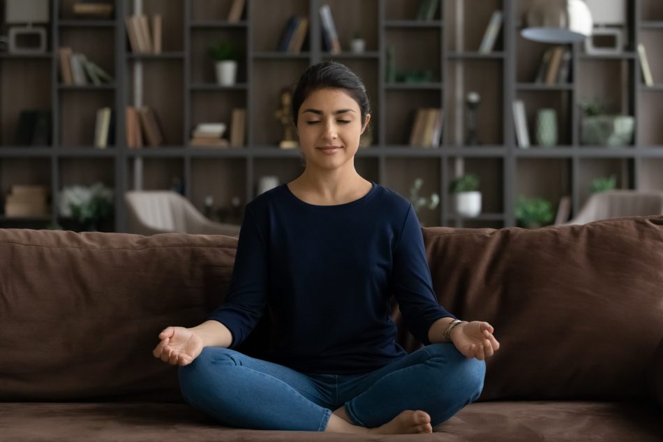 young Indian woman meditates with eyes closed on couch