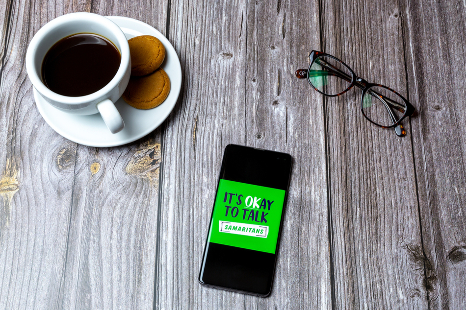 Samaritans interface on smart phone lying on a table next to reading glasses and a cup of coffee