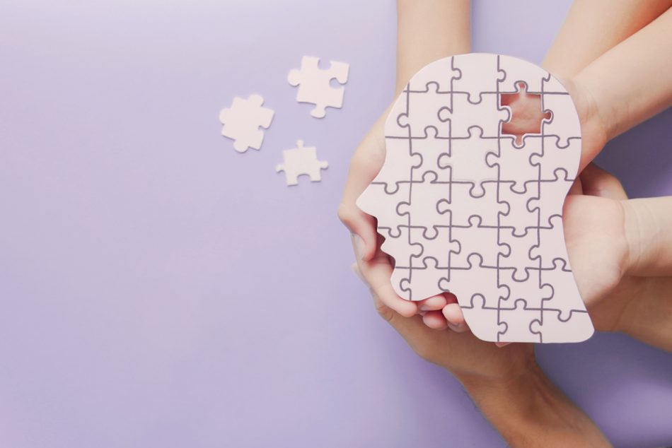 People holding their hands together to hold a jigsaw of a face with a puzzle piece to represent the international effort of the schizophrenia study.