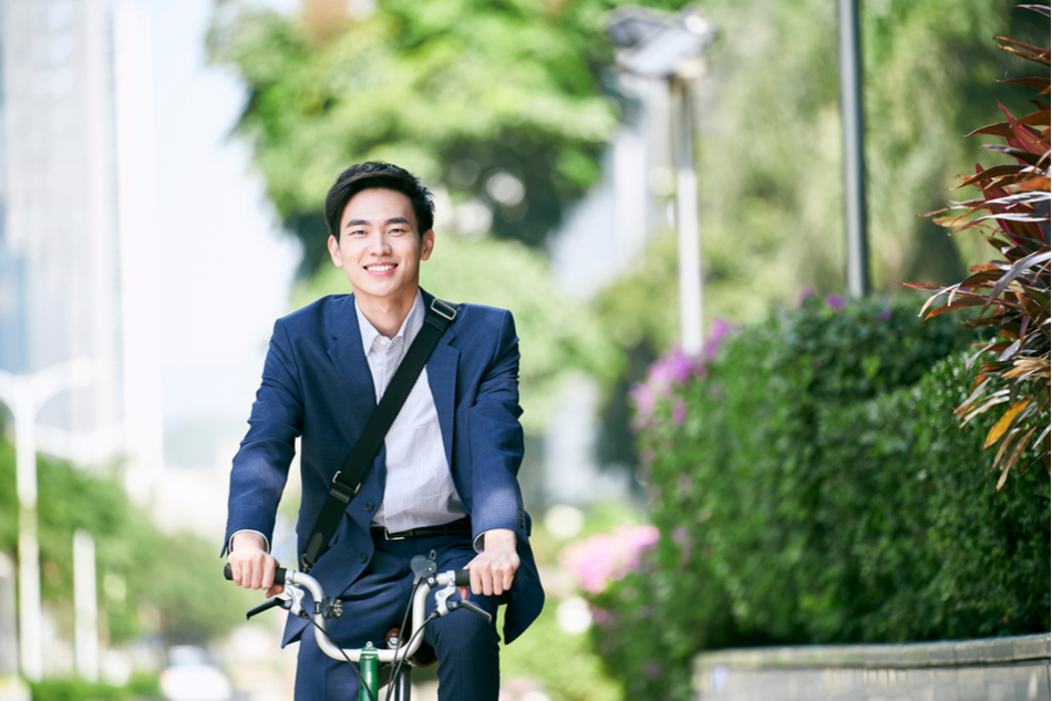 Asian man bikes through city street lined with bushes and trees