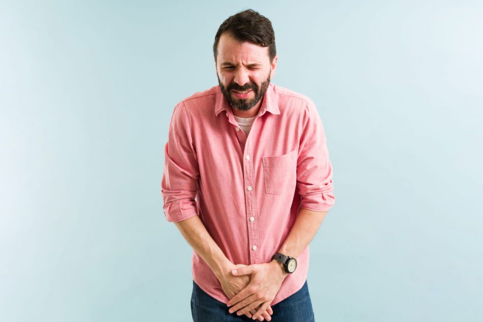 Man in pink shirt clutches bladder area in pain against a light blue background
