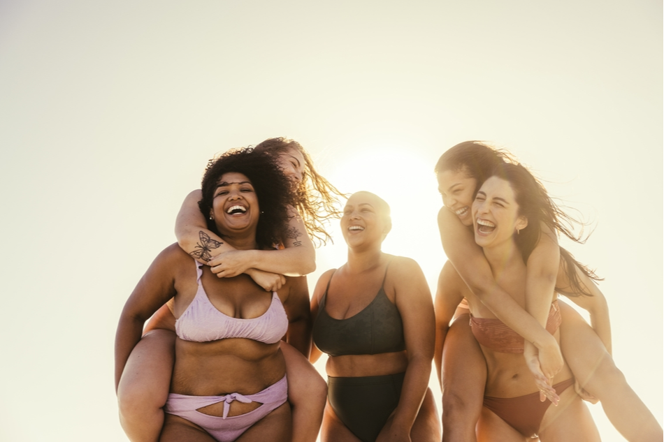 five diverse girl friends laugh and give each other piggybacks in the sun
