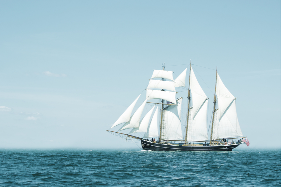 Three-masted schooner sailing at sea on clear sunny day