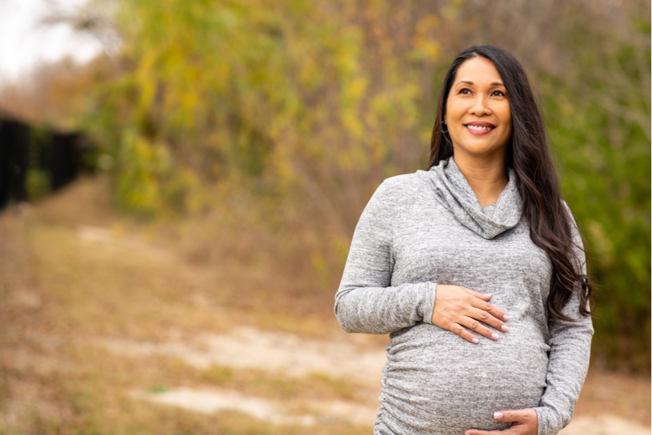 older Asian pregnant woman walks outside in nature