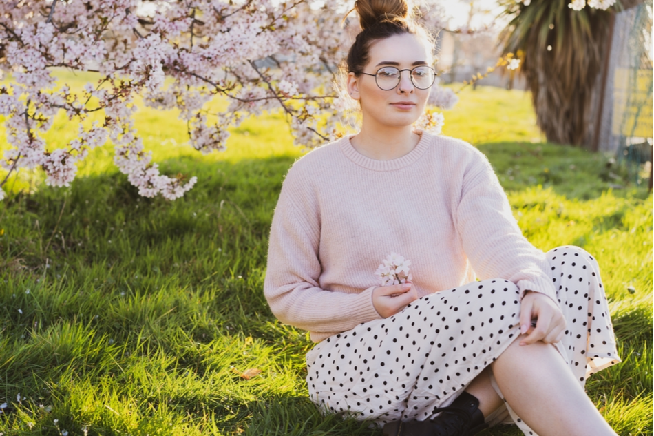young white woman with glasses sits outside under a blossoming tree