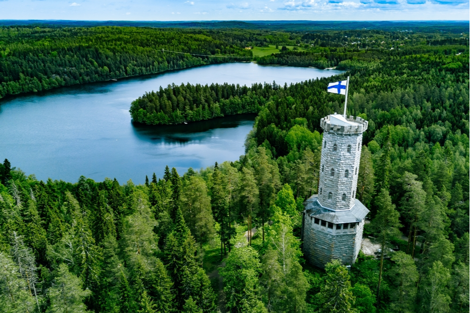 Aerial view of observation tower with Finnish flag among blue lakes and green forests in summer Finland.