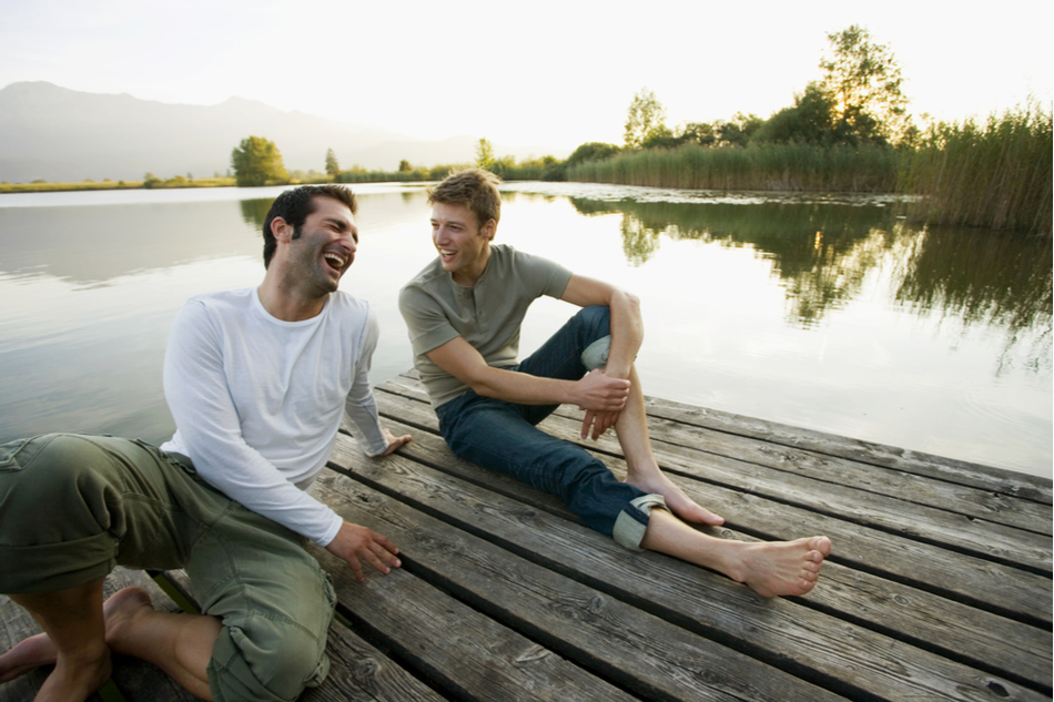 two young male friends chat with each other on a dock
