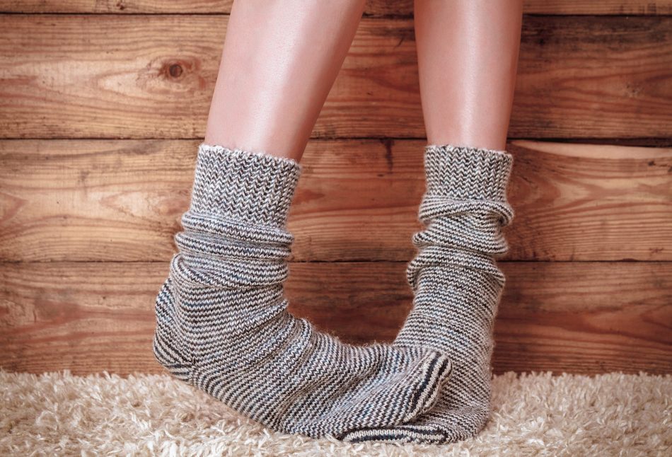 Legs of a woman in gray socks on the carpet on the wooden background. Vintage toning