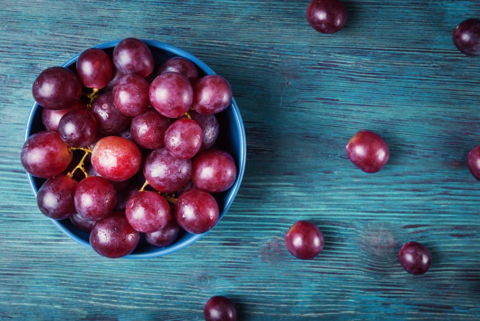 Bowl of red grapes on blue wooden table.