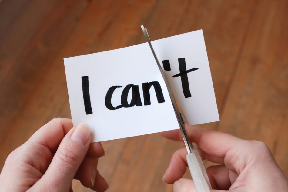 Person cutting a piece of paper with I can / can't as a representation of finding confidence.