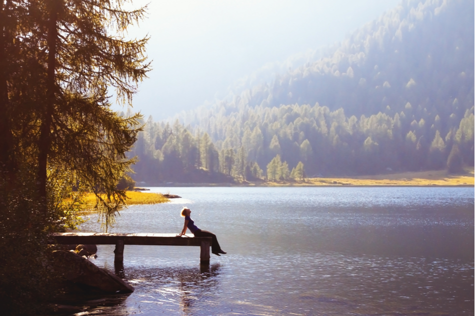 happy joyful young woman sitting on dock overlooking lake and forests