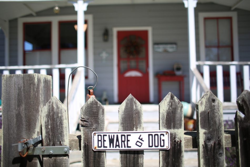 Beware of Dog sign for security on wooden fence outside of home grey ranch house with red door.