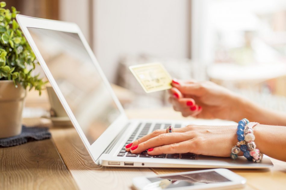 woman poised to shop online with credit card in hand and laptop open on desk