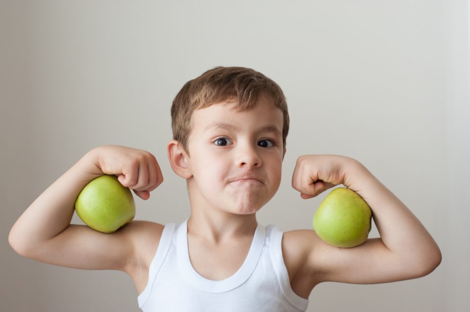 Young child with green apples between his biceps.