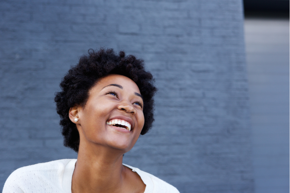 young beautiful Black woman smiles and looks away against blue brick backdrop