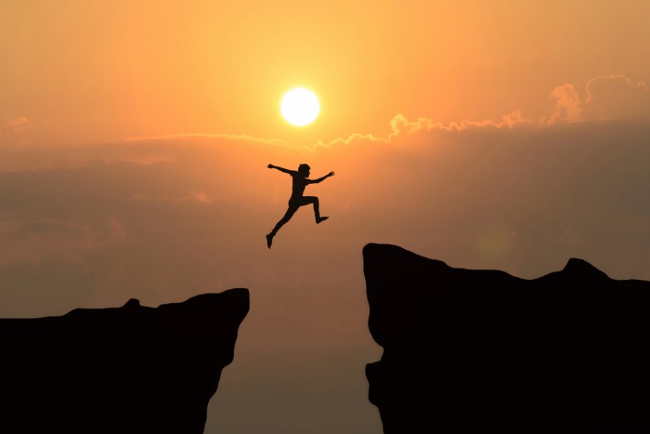 Man jump through the gap between hill.man jumping over cliff on sunset displaying courage.