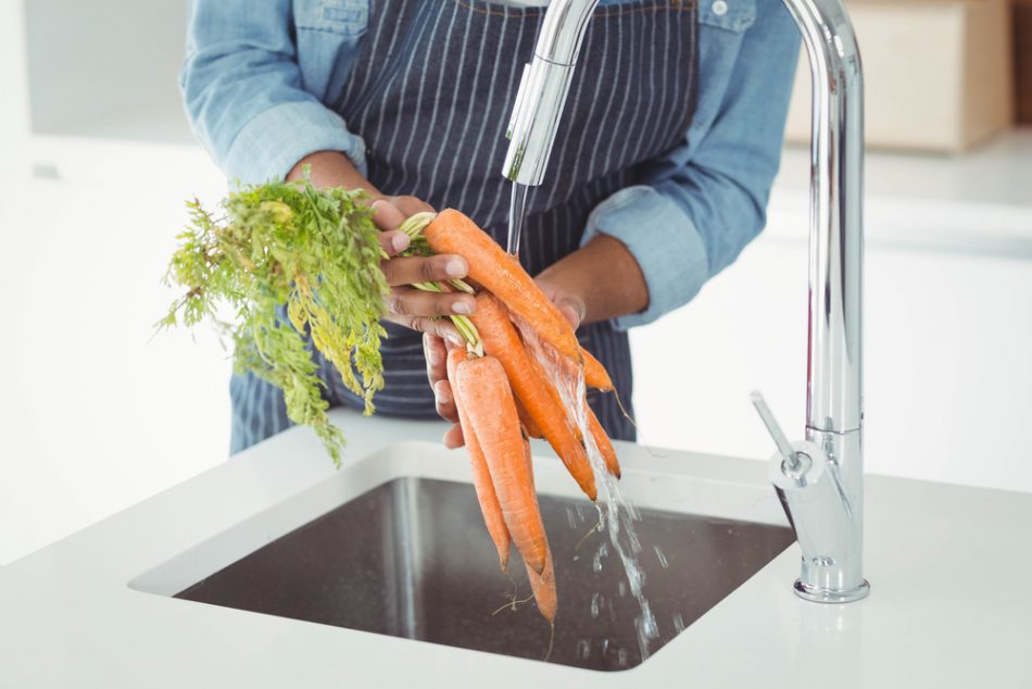 Person wearing a striped apron washing unpeeled carrots.