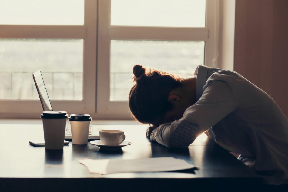 Overworked tired businesswoman sleeping on table in office suffering from fatigue with coffee in front of her.