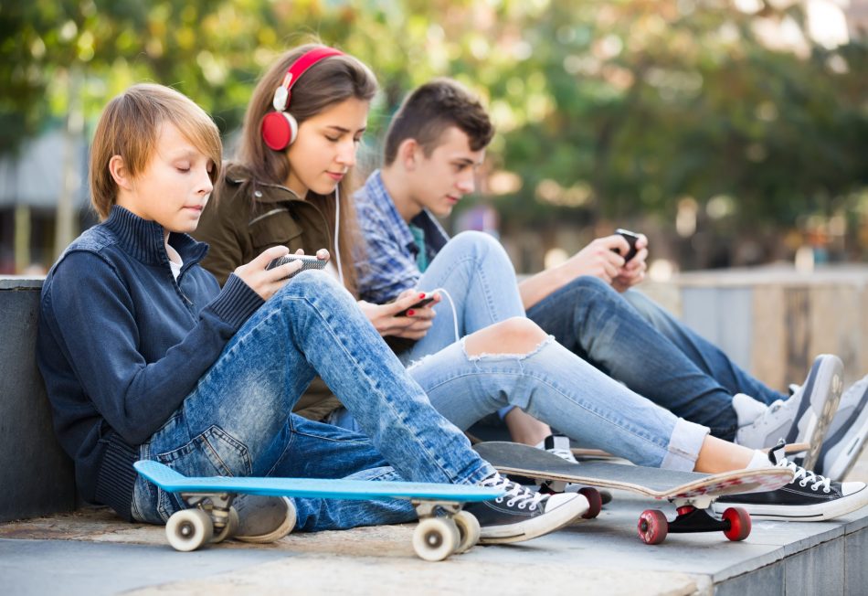 Group of teenage friends in casual relaxing with mobile phones outdoor