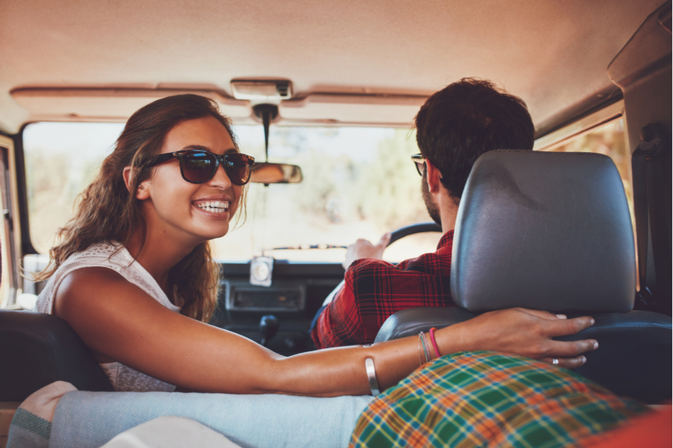 Happy young woman looking back with man driving car. Couple in a car going on roadtrip.