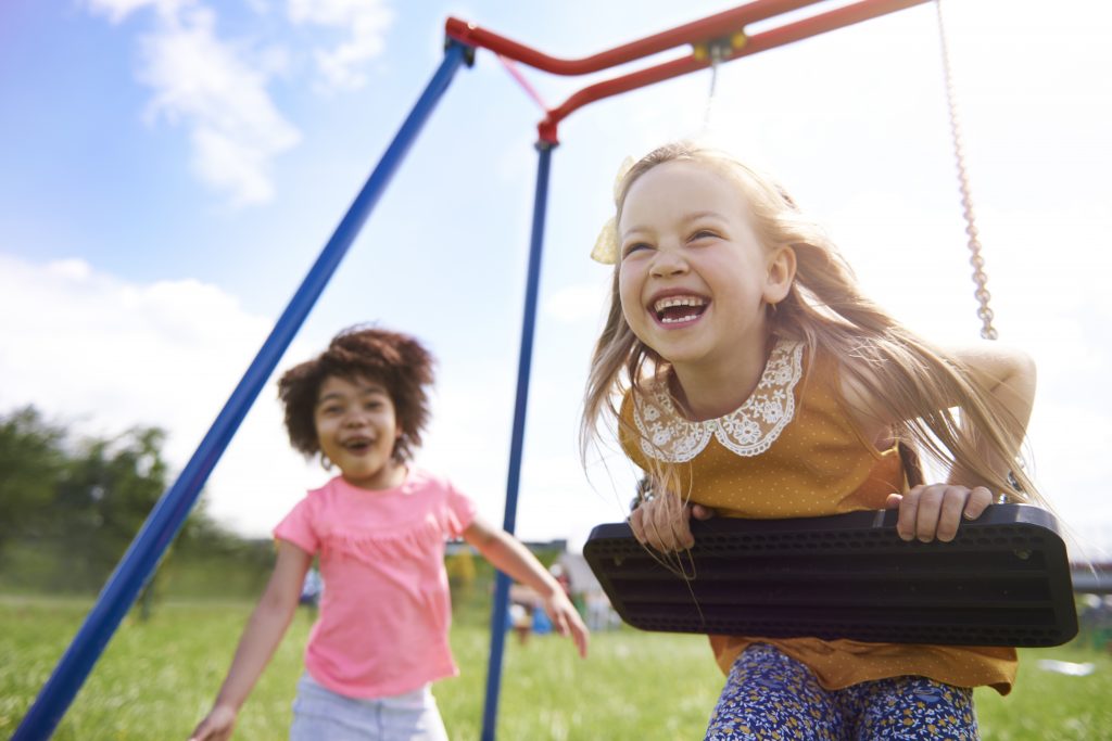 two young girls play happily on an outdoor swing set