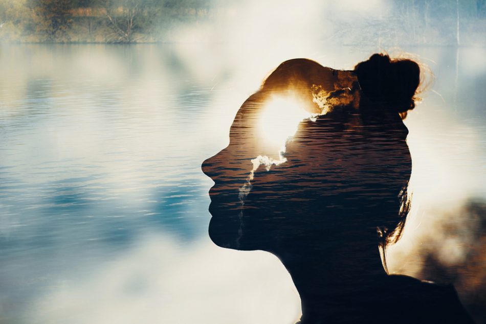 Person with hair in a bun, photoshopped sun on their head with clouds and gentle water in the background.