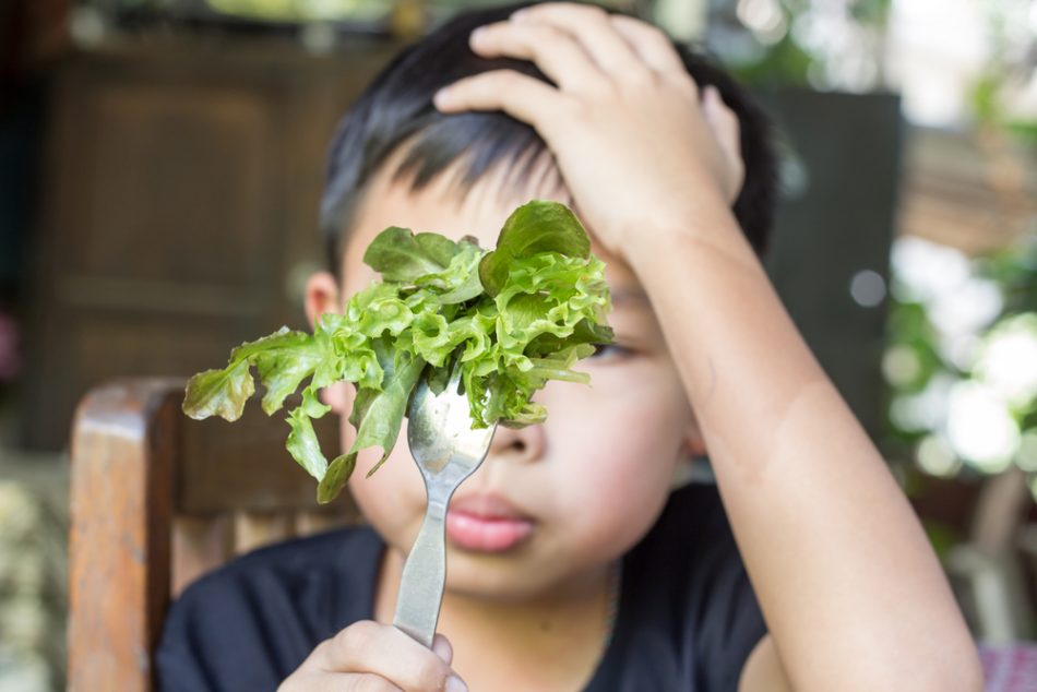 Unhappy child looks at fork of lettuce